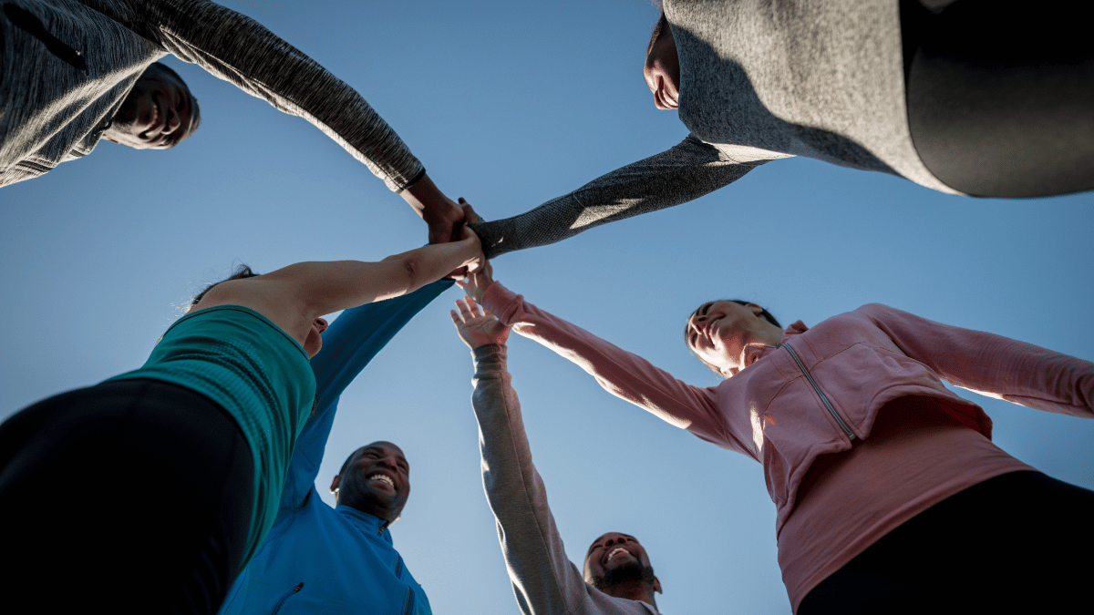 Ekipa ljudi na team building dogodku skupaj dviguje roke v zrak